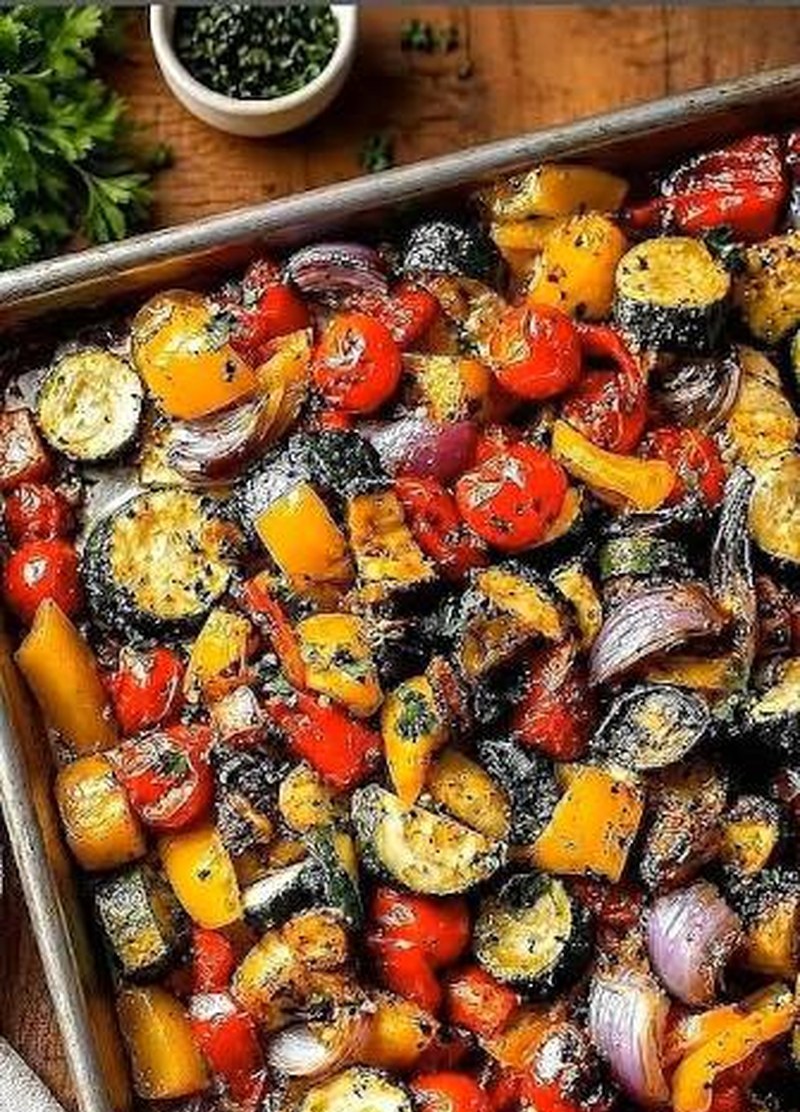 Colorful roasted vegetables on a sheet pan—zucchini, peppers, cherry tomatoes, and red onion with fresh herbs